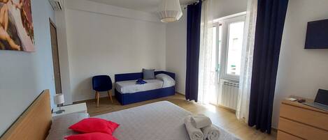 A bedroom with a bed, a desk, a chair, a window with curtains, and a painting on the wall.