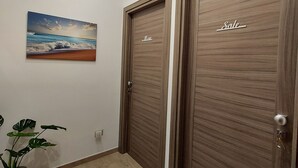 A hallway with two wooden doors labeled "Sole," a ceiling-mounted air conditioner, a potted plant, and a painting of a beach scene. - Sapore di Mare Holidays (Maiori)