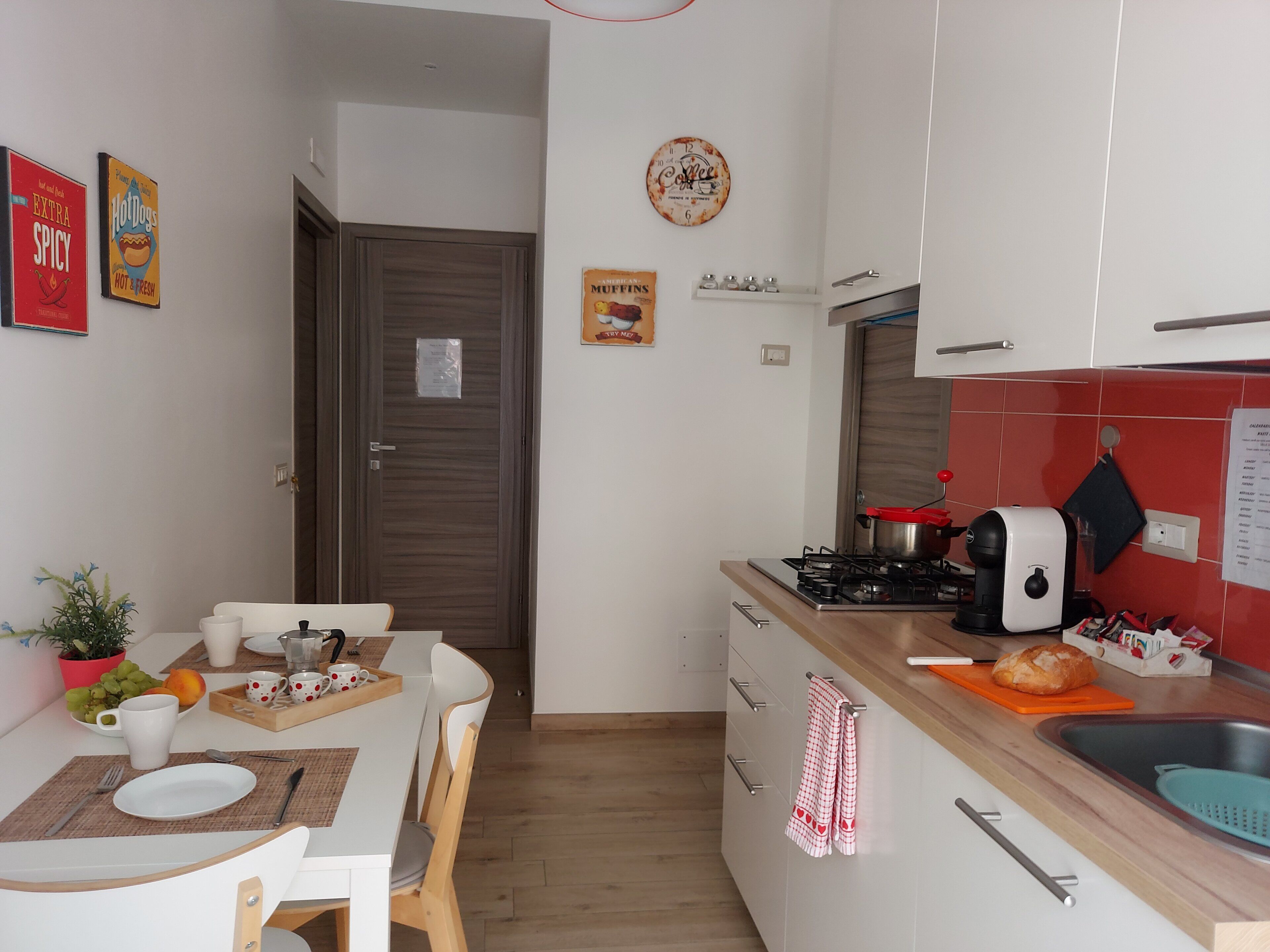 A compact kitchen with a dining area, a stove, a coffee maker, and a clock on the wall.
