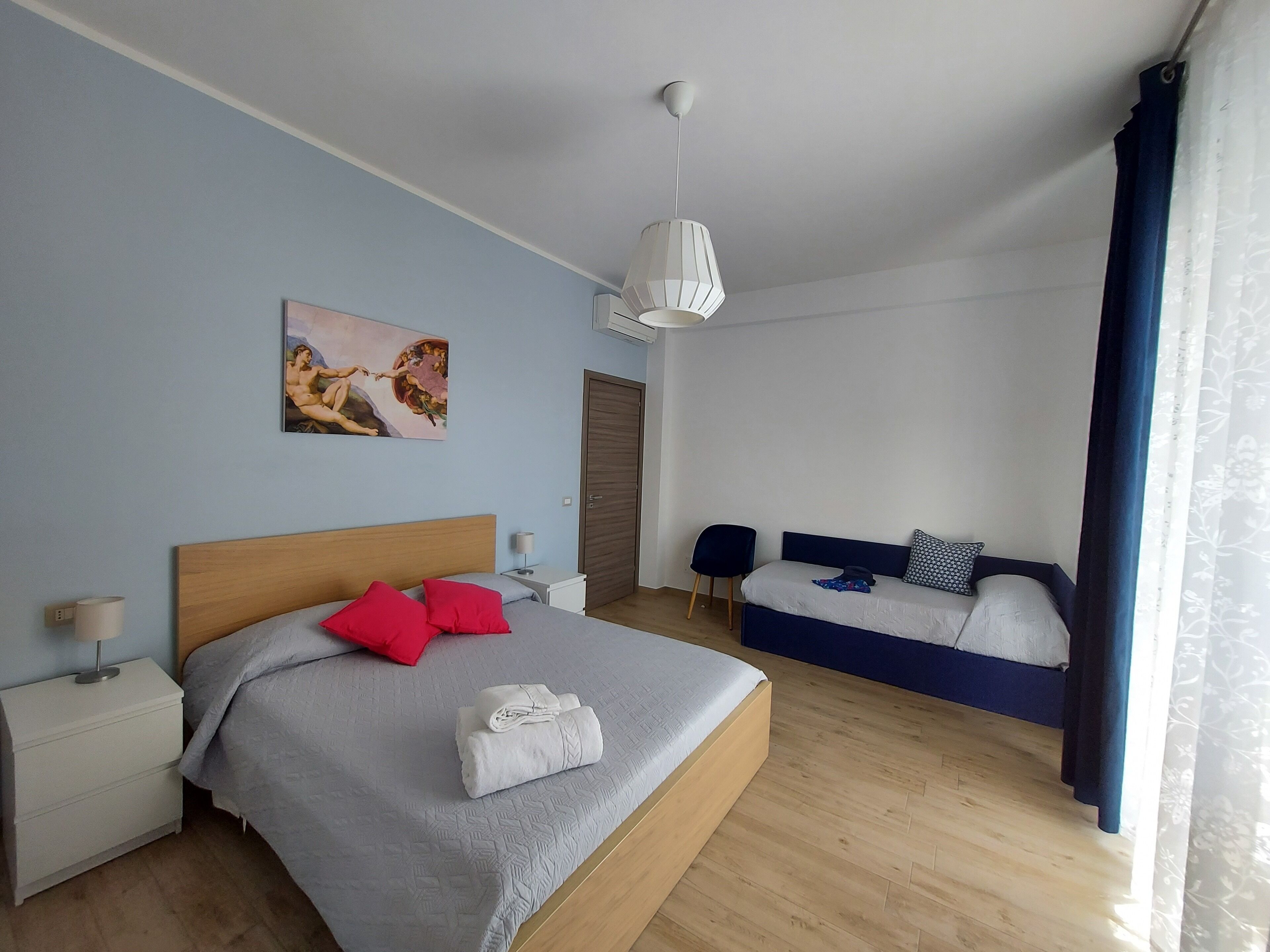 Une chambre moderne avec un grand lit, un petit canapé, un tableau au mur et une fenêtre avec des rideaux.