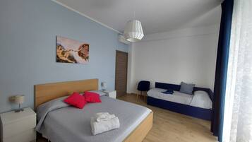 Une chambre moderne avec un grand lit, un petit canapé, un tableau au mur et une fenêtre avec des rideaux.