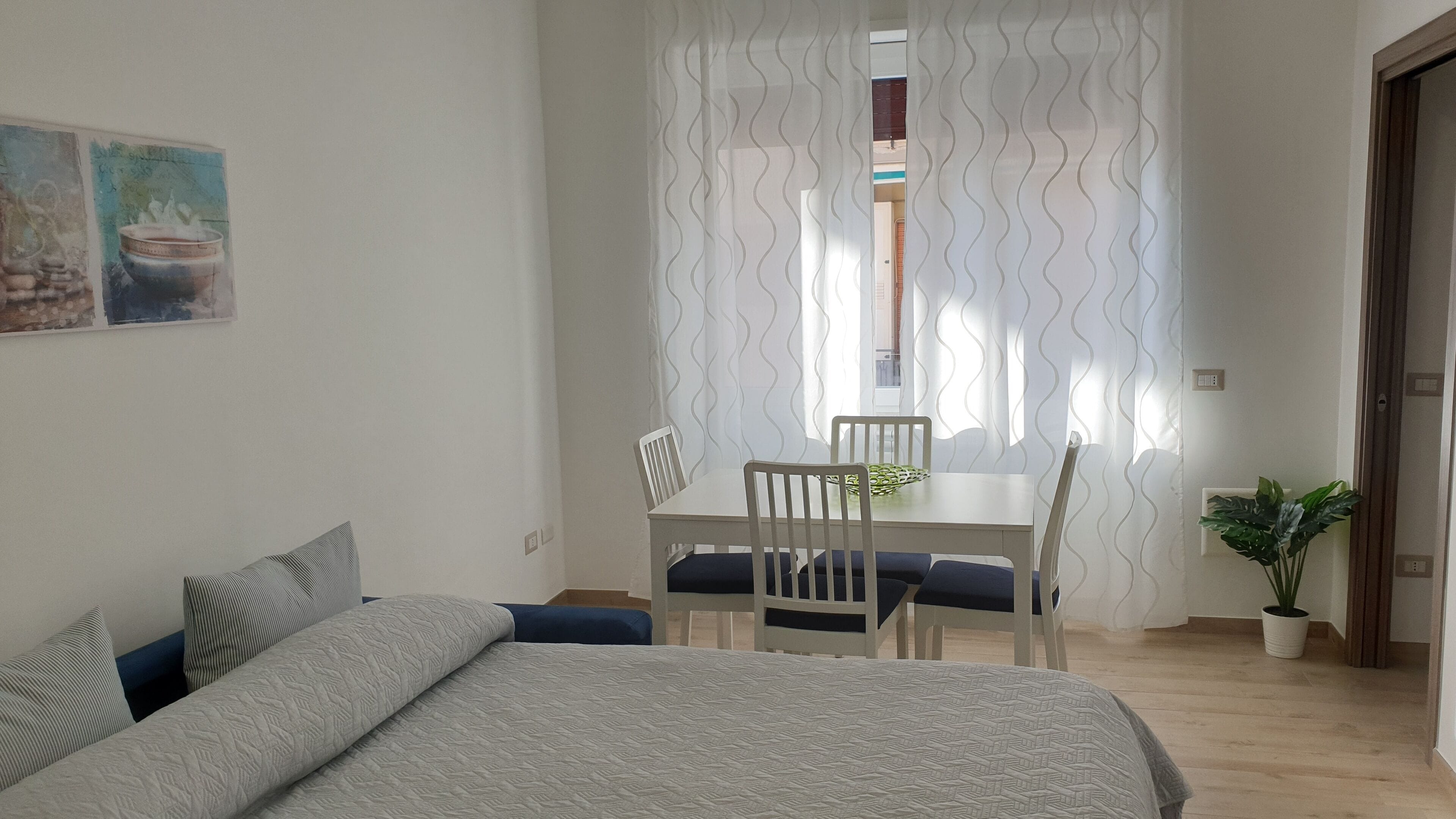 Une chambre à coucher avec un lit, une table à manger avec des chaises, une plante en pot et une fenêtre avec des rideaux.