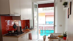 A modern kitchen with white cabinets, a red pendant light, and a dining area with a table and chairs. - Sapore di Mare Holidays (Maiori)