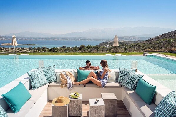 A poolside seating area with a view of the sea and mountains.