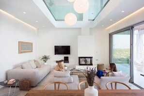 A modern living room with a sofa, coffee table, and chairs. There is a TV mounted on the wall and a fireplace.