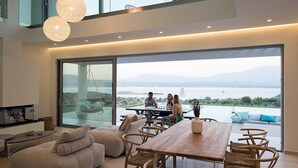 Un salón moderno con una gran mesa de comedor, asientos cómodos y vistas a una masa de agua a través de amplios ventanales.
