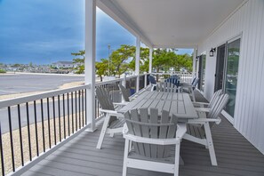 A covered outdoor seating area with a table and chairs, overlooking a parking lot and a view of the ocean.