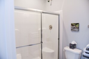 A bathroom with a glass shower enclosure, a toilet, and a framed picture on the wall.