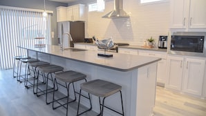 A modern kitchen with a central island, bar stools, stainless steel appliances, and white cabinetry. - Family fun-beach, marina, pools, pet friendly! (Long Neck)