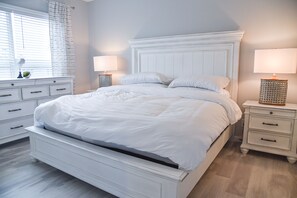 A white bed with a wooden headboard, two bedside tables with lamps, and a window with blinds.