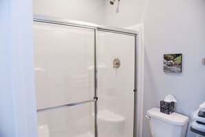 A bathroom with a glass shower enclosure, a toilet, and a framed picture on the wall.
