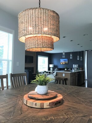 A dining area with a round wooden table, a woven pendant light, and a potted plant.