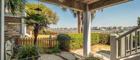 A covered outdoor area with a wooden ceiling, a wooden fence, and a view of a marina with boats and buildings in the background.