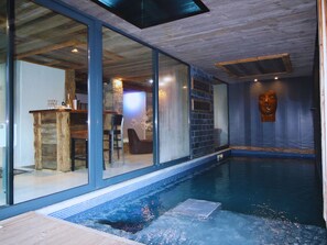 A modern indoor swimming pool with a glass wall, wooden flooring, and a stone wall. - Large chalet in Vars for 19 people—indoor pool, spa, movie theater, mountain views (Vars)