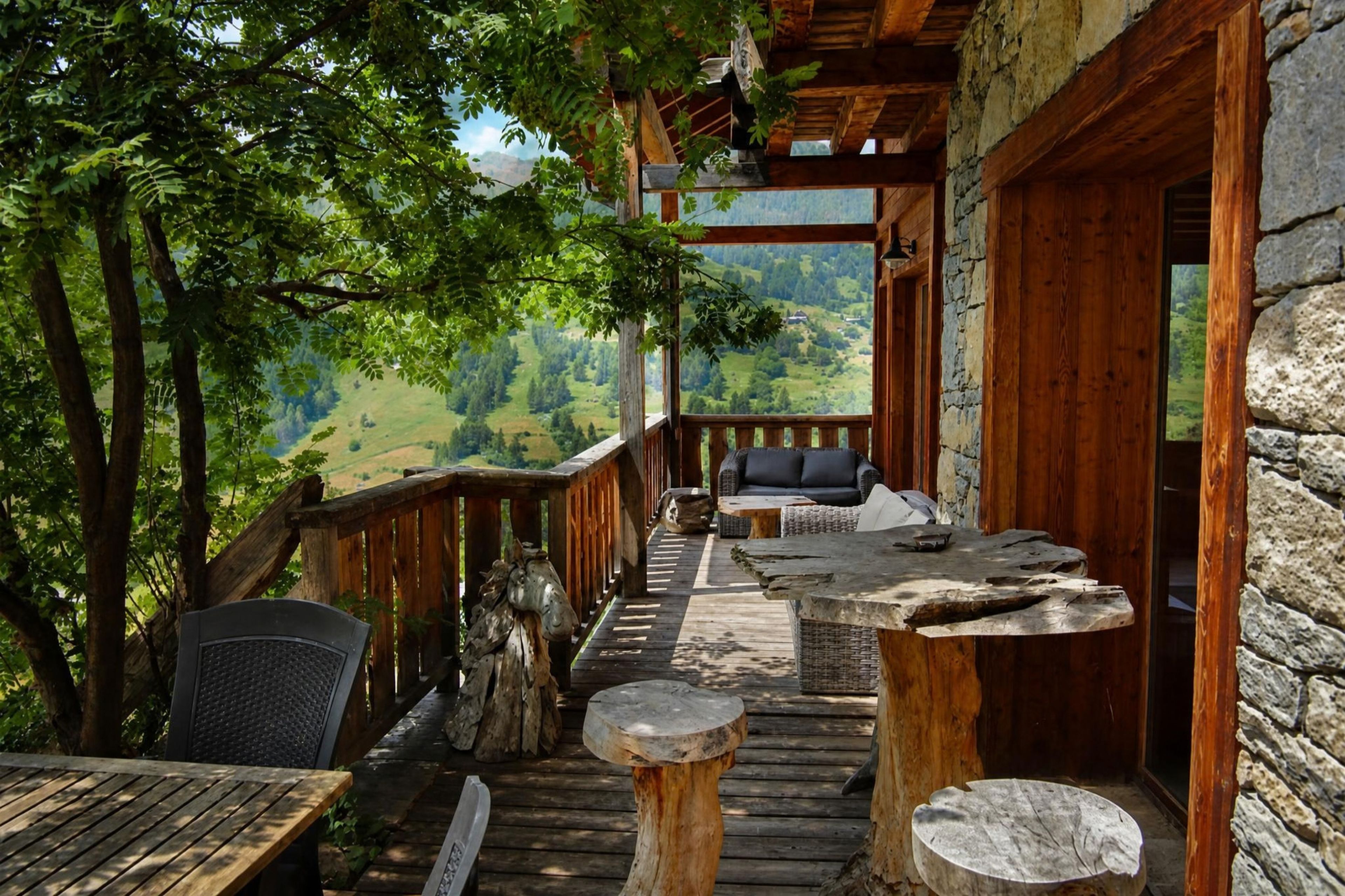 An outdoor wooden deck with a stone wall, a wooden bench, and a table.