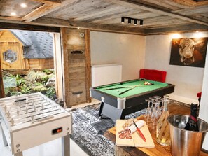 A pool table with billiard balls, a foosball table, and a table with sliced salami and wine glasses.