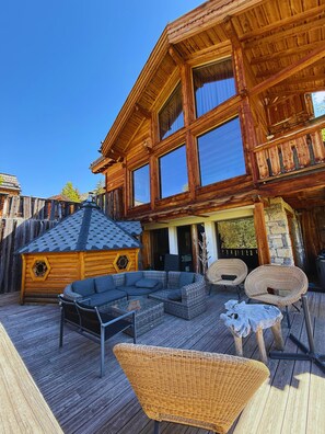 A log cabin with a deck, outdoor seating, and a hexagonal window. - Large chalet in Vars for 19 people—indoor pool, spa, movie theater, mountain views (Vars)
