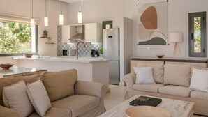 A modern kitchen with pendant lighting, a central island, and a dining area with a sofa and coffee table. - Villa Rodia (Kefalonia)