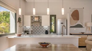 A modern kitchen with pendant lights, a central island, and a view of the outdoors. - Villa Rodia (Kefalonia)