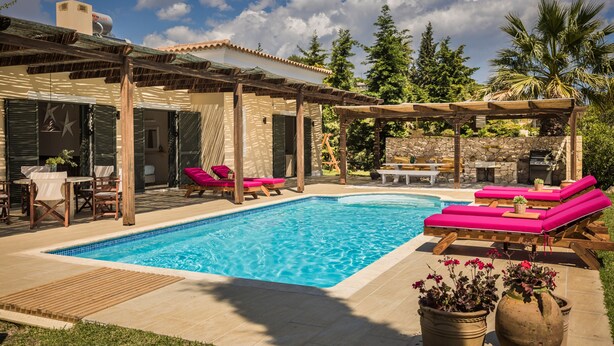 A swimming pool with lounge chairs, a pergola, and a stone wall. - Villa Rodia (Kefalonia)