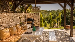 An outdoor patio with a stone wall, a wooden pergola, a white table, and a leather sofa. - Villa Rodia (Kefalonia)
