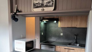 Une cuisine compacte équipée d’un four à micro-ondes, d’une cuisinière et d’un évier. Un petit coin repas avec une table et des chaises est également disponible.