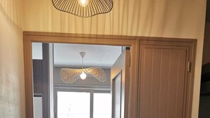 Un couloir menant à une chambre dotée d’une fenêtre, d’un banc et d’une armoire.