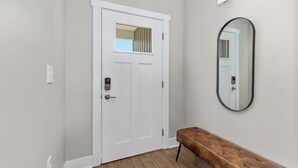 A hallway with a white door, a bench, and a wall-mounted mirror. - Relax in Comfort! 2BR Condo Close to Grand Rapids (Wyoming)