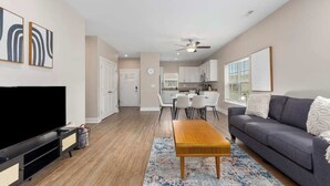 A modern living room with a flat-screen TV, a wooden coffee table, a gray sofa, and a dining area with a white table and chairs. - Relax in Comfort! 2BR Condo Close to Grand Rapids (Wyoming)