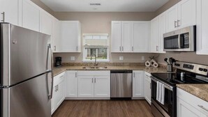 A modern kitchen with white cabinets, stainless steel appliances, and a granite countertop. - Relax in Comfort! 2BR Condo Close to Grand Rapids (Wyoming)