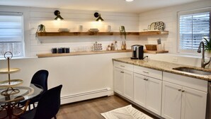 A modern kitchen with white cabinetry, a granite countertop, and a dining area with a round table and chairs.