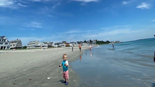 A beach with a clear sky and a child walking on the sand.