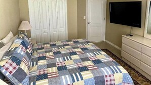 Une chambre à coucher avec un lit, un ventilateur de plafond, une télévision et une commode.