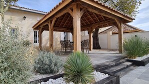A wooden pergola with a tiled roof, surrounded by a garden with various plants and a seating area with chairs. - Luxury 5* cottage with own private heated pool - Sleep 4 (Villegouge)