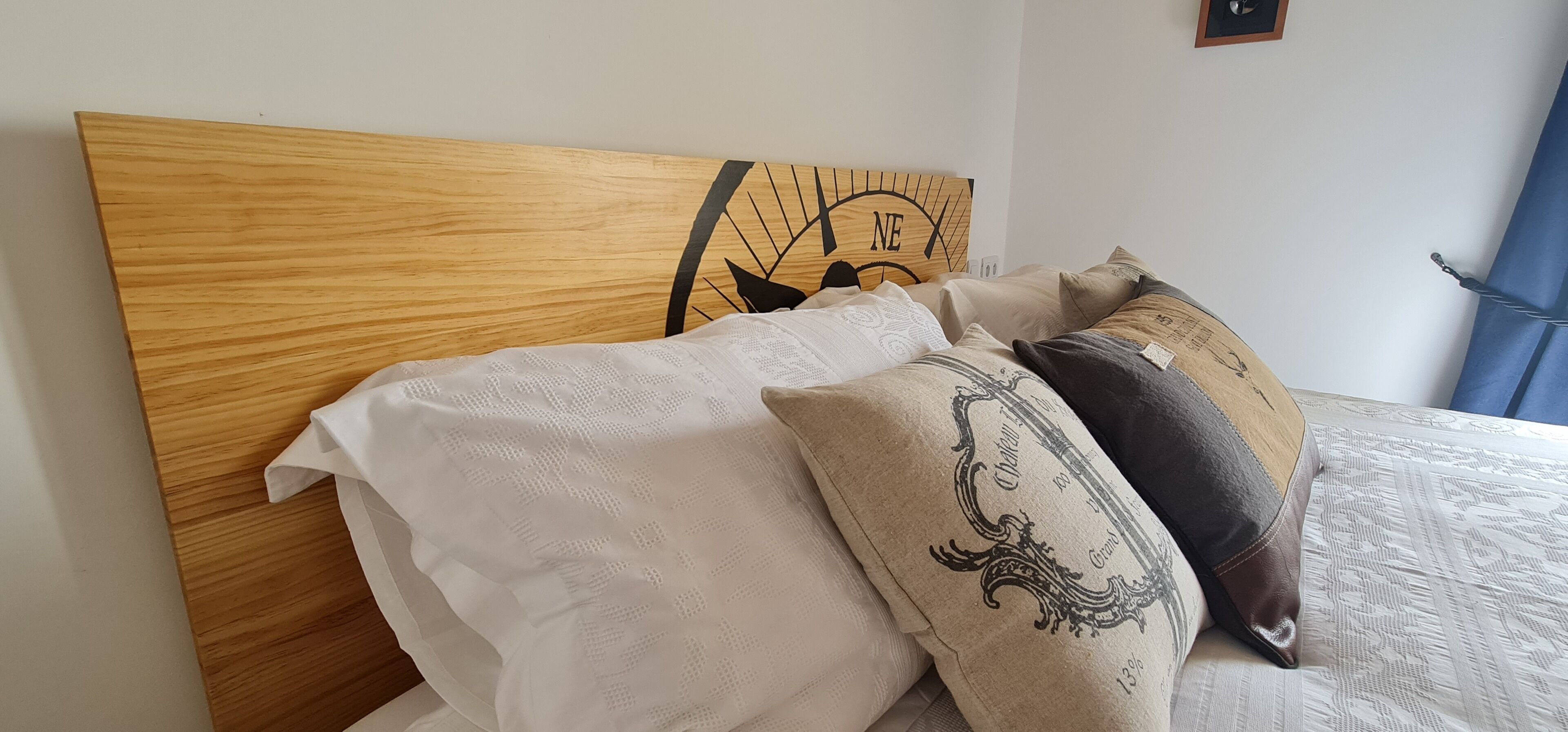 A bed with a wooden headboard, white and patterned pillows, and a wall-mounted clock.
