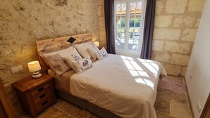 A bedroom with a stone wall, a wooden headboard, a bed with white bedding, and a nightstand with a lamp. - Luxury 5* cottage with own private heated pool - Sleep 4 (Villegouge)