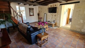 A cozy living room with a black leather sofa, a wooden coffee table with a vase of flowers, and a staircase leading to an upper floor. - Luxury 5* cottage with own private heated pool - Sleep 4 (Villegouge)