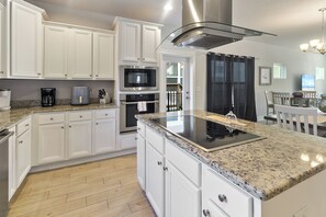 A modern kitchen with white cabinetry, a stainless steel range hood, a built-in microwave, and a granite countertop.