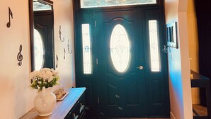 Techo de madera con candelabro, puerta negra con vidrieras, un espejo y un florero con flores sobre un aparador.