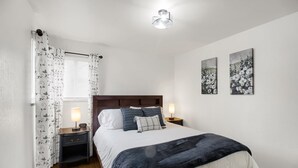 Une chambre à coucher bien rangée, avec un lit, deux tables de chevet avec des lampes, une commode et une fenêtre avec des rideaux.