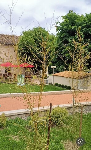 A garden area with a paved walkway, a building with a tiled roof, and a red umbrella.