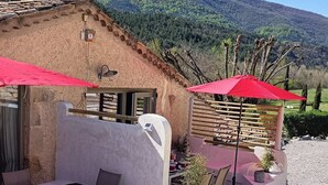 A rustic building with a sloped roof, a wooden fence, and a red umbrella. - Gîte DE LA Source (Barret-sur-Méouge)