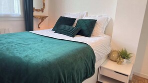 A bed with a green blanket, white pillows, and a nightstand with a plant and decorative items.
