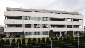 A multi-story building with balconies, a paved driveway, and neatly trimmed hedges. - Ferienwohnung Hirschen (Gossau)