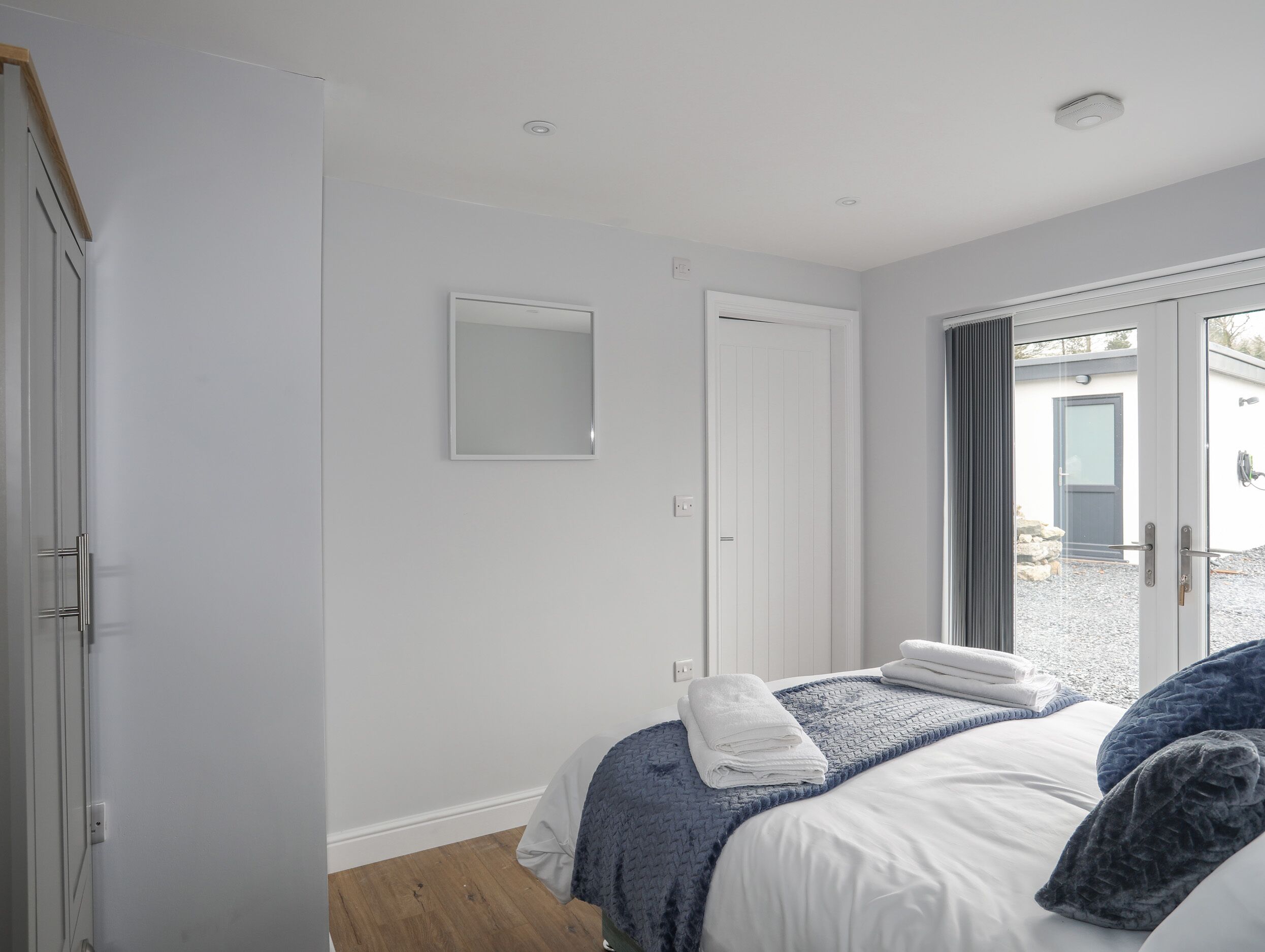 Ett sovrum med en säng, en dörr, en spegel och ett fönster.