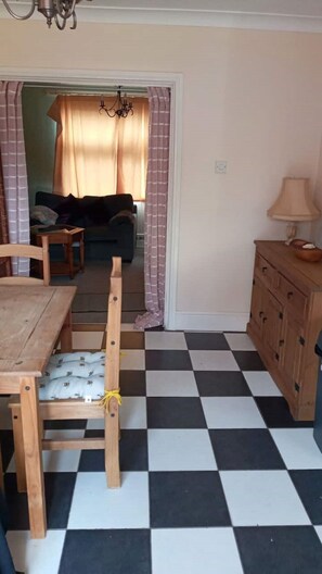 A dining area with a checkered floor, wooden chairs, a table, and a cabinet.
