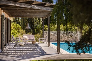 A covered outdoor area with a pool, lounge chairs, and a pergola.