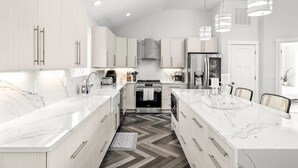 Une cuisine moderne avec des meubles blancs, un îlot central et un sol décoré d’un motif en chevrons.