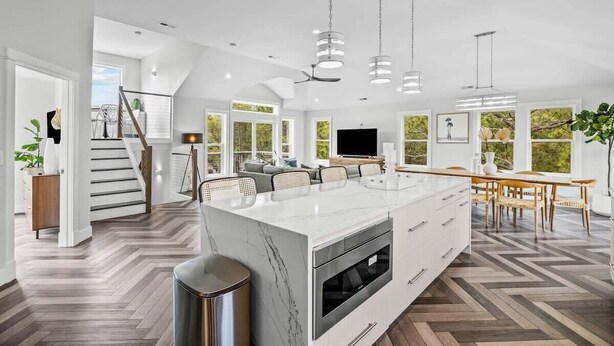Une cuisine spacieuse dotée d’un grand îlot central, d’un éclairage moderne suspendu et d’un parquet en bois disposé en chevrons.