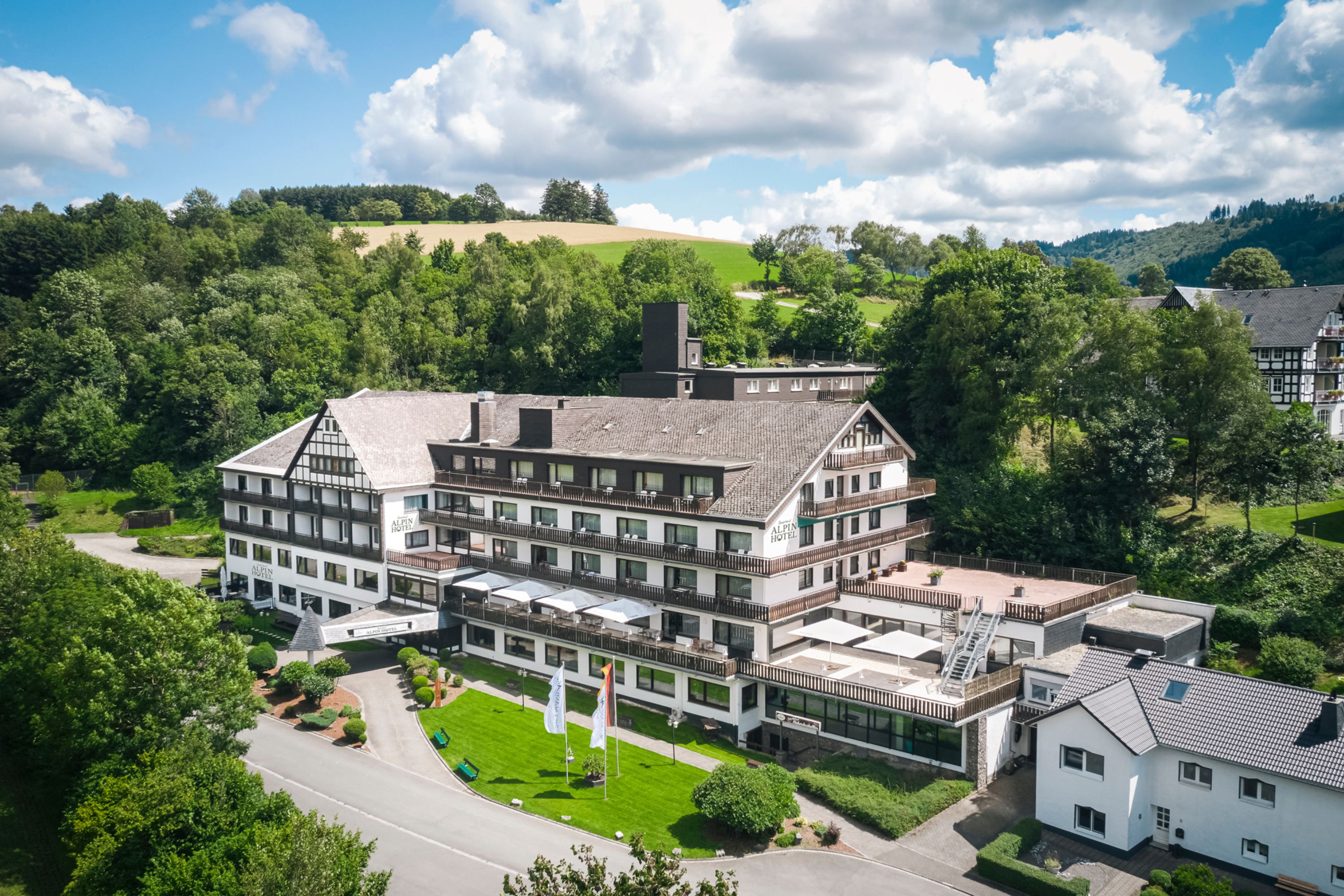 Ein großes Hotel mit mehreren Etagen, einem zentralen Innenhof und einer umliegenden, üppigen Grünanlage.